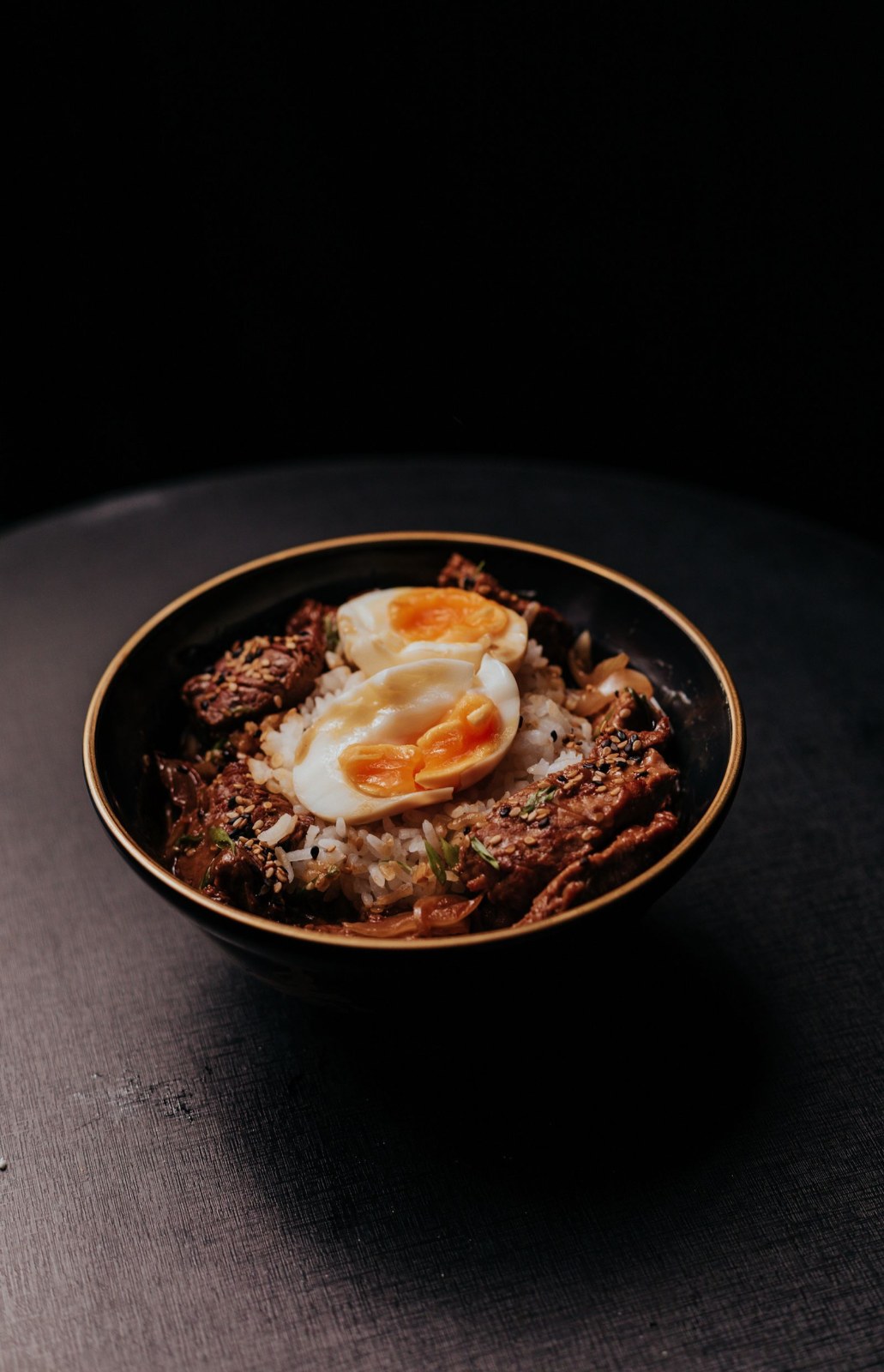 Caramelised beef over rice with soft eggs in a dark bowl