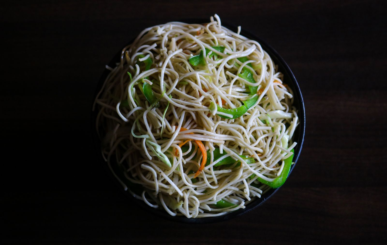 Wok-tossed noodles with spring onion in a black bowl